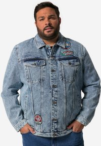 Chaqueta de mezclilla de color azul claro con cierre de botones, dos bolsillos en el pecho y parches bordados. Mangas largas con puño, corte relajado y un ligero desgaste.