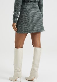 Mini falda corta de cuadros grises con cintura ajustada y tejido texturizado, combinada con botas de tacón alto de cuero blanco.