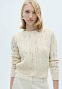 Cremfarbener Strickpullover mit Zopfmuster, geripptem Ausschnitt und Bündchen sowie einem leicht verkürzten Schnitt. Sanfte Textur.