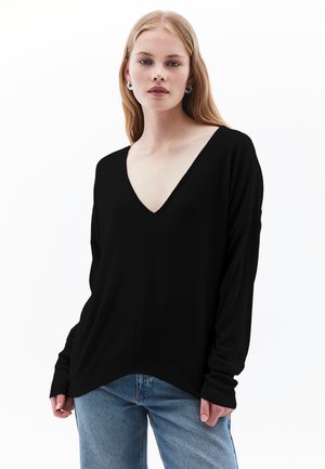 Haut noir à manches longues et col en V, avec une coupe décontractée et des poignets côtelés ; associé à un jean bleu clair. Tissu doux, design simple.