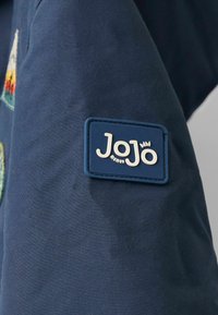 Jūras spēku audums ar izstrādātiem rakstiem, kam ir zils gumijas uzlīme, uz kuras baltajiem burtiem ir rakstīts "JoJo bébé". Ievērojams ar savu rotaļīgo zīmola identitāti.