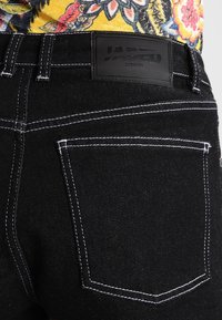 Svarta jean med vit sömnad, med en märkesläderpatch på midjan och vanliga bakfickor.