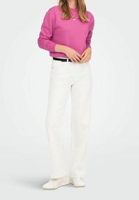 Sudadera fucsia de manga larga, combinada con pantalones blancos de corte recto y zapatillas blancas. Diseño sencillo sin patrones destacados.