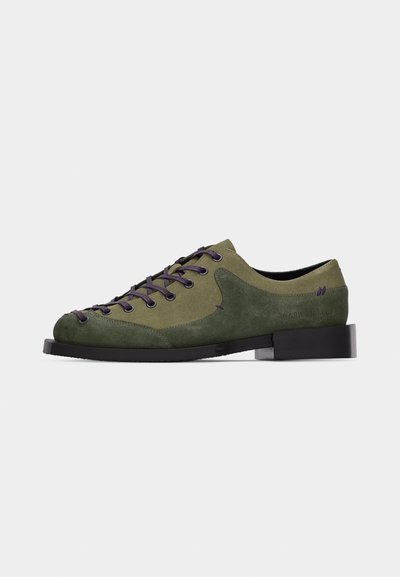 Low-profile olive green suede shoe with dark laces, black sole, and thick heel, shown against a plain light background.