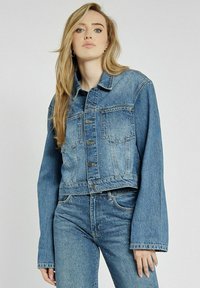 Jasnoniebieska kurtka dżinsowa o skróconym kroju z zapięciem na guziki, kieszeniami na piersi i długimi rękawami. W zestawie ze zużytymi jasnoniebieskimi dżinsami.