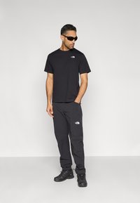 T-shirt noir et pantalon assorti avec le logo The North Face. Portés avec des lunettes de soleil noires et des baskets noires robustes. Design simple et fonctionnel.