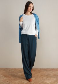 Biała bluzka z długim rękawem i okrągłym dekoltem, zestawiona z granatowymi spodniami o szerokich nogawkach. Jasnoniebieski kardigan narzucony na jedno ramię; pomarańczowe czółenka.