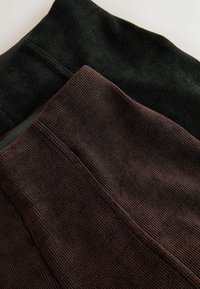 Twee geribbelde knit leggings liggen plat, één zwart en één donkerbruin, en tonen een elastische tailleband en een getextureerde stof.