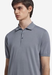 Ljusgrå polo skjorta gjord av ett slätt stickat tyg, med en dubbelknäppning och korta ärmar med ribbade muddar.