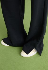 Schwarze, weit geschnittene Sweatpants mit glatter Textur, kombiniert mit hellen Sneakers. Die Hosenbeine fallen dezent über die Schuhe.