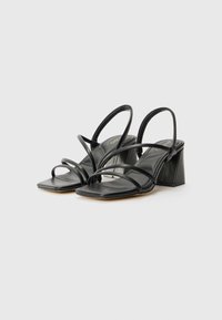 Sandale cu toc negru, cu toc bloc înclinat, vârf pătrat și multiple curele subțiri pe instep. Textură de piele netedă, design minimalist.