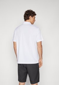 White polo shirt with a collar, short sleeves, and a relaxed fit; paired with dark gray shorts. Smooth texture and simple design.