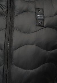 Μαύρο καπιτονέ ύφασμα με οριζόντια ραφή κυματιστή και κάθετο φερμουάρ, με μια μικρή μαύρη ετικέτα που γράφει "Blauer U.S.A."