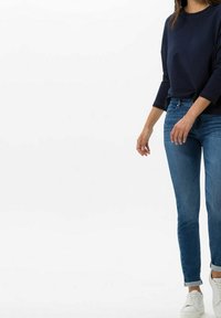 Sudadera azul marino con mangas tres cuartos combinada con vaqueros de mezclilla azul claro. Zapatillas blancas completan el conjunto informal.