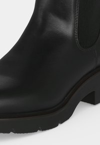 Bottine en cuir noir avec talon épais et panneau latéral élastique, avec une finition lisse et polie et une semelle texturée.