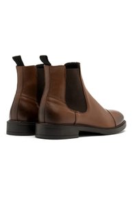 Brązowe skórzane botki Chelsea z elastycznymi panelami bocznymi i pętlami do wciągania, z zaokrąglonym noskiem i niskim czarnym obcasem. Gładkie wykończenie z minimalnym przeszyciem.