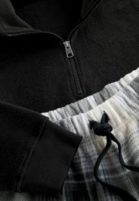 Musttohune musta kangastagi eesltukiga; halli ja valge mustriga spordipüksid elastse vöökoha ja sidumisega.