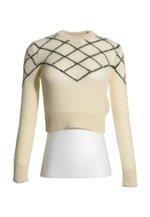 Jersey de punto de color crema con mangas largas y patrón de diamantes negros en el pecho y los hombros sobre un torso de maniquí blanco.