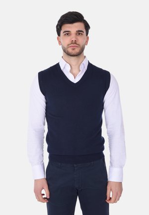 Gilet in lana blu navy con scollatura a V, indossato sopra una camicia bianca con bottoni. Presenta polsini e orlo a coste per struttura e vestibilità.