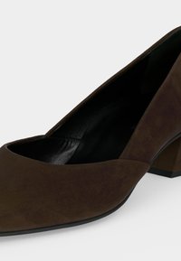 Escarpin femme en daim marron à petit talon, bout fermé et silhouette légèrement arrondie sur fond blanc.