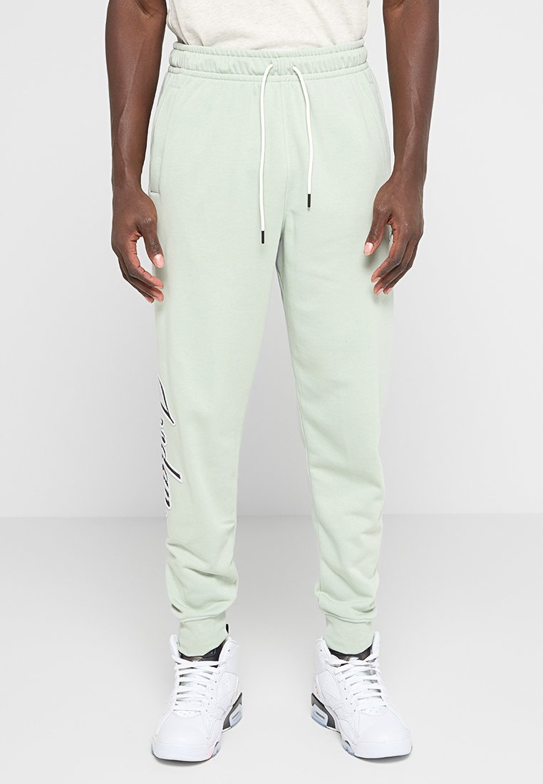 Pantaloni jogger verde chiaro con una cintura elastica, cordoncino e dettaglio di testo stampato sulla gamba sinistra. Realizzati in tessuto morbido.