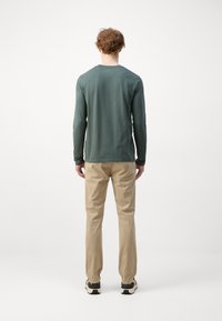 Langærmet, mørkegrøn skjorte med rund hals, parret med beige bukser. Sættet har en afslappet pasform og minimalistisk design uden synlige mønstre.