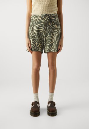 Pantalones cortos verdes con un patrón de hojas, con un lazo en la cintura. Combinados con zapatos marrones y calcetines gris claro. Parte superior de punto texturizado.
