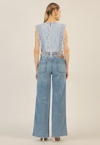 Helles blaues Spitzentop mit gewellten Kanten und einem Reißverschluss im Rücken, kombiniert mit hellen, weiter geschnittenen Denim-Jeans mit Gesäßtaschen.