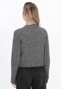 Pulover gri tricotat cu decolteu rotund, mâneci lungi și un design scurt. Textura pare moale și ușor pufoasă.