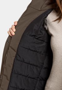 Brun polstret jakke med sort kant, der har en glat overflade, sølv lynlås og kviltet tekstur på den indre stof.