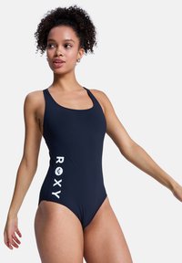 Maillot de bain une pièce bleu marine en matière lisse avec un col arrondi, arborant le logo blanc "ROXY" le long du côté.