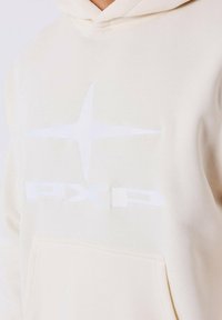 Crème-kleurige hoodie met een zachte textuur. Uitrusting met een grote witte geborduurde ster en het "PXP"-logo aan de voorkant. Inclusief een kangoeroezak.
