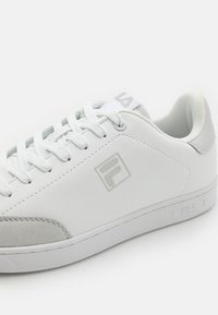 Zapatilla blanca de cuero con acentos de ante gris, cordones planos y suela cosida. Logo de Fila grabado en el costado y la lengüeta.