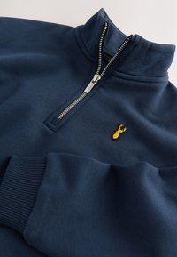Navy blue sweatshirt with a high collar, zippered front, ribbed cuffs, and a yellow embroidered lobster logo on the chest. Smooth texture.