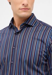 Camicia button-up a righe con linee verticali in blu scuro, rosso e blu chiaro su un tessuto liscio; colletto classico e due bottoni decorativi.