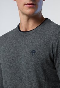 Suéter de lana gris con escote redondo, ribetes en azul oscuro y un pequeño logotipo circular bordado en azul marino en el pecho.