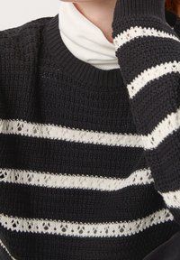 Schwarzer gestrickter Pullover mit horizontalen weißen Streifen und floralen Spitzelementen. Gerippter Kragen und Bündchen. Strukturiertes Material sorgt für visuelles Interesse.