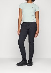 T-shirt manches courtes vert menthe avec un petit logo noir, associé à un pantalon noir slim et des chaussures de sport noires.