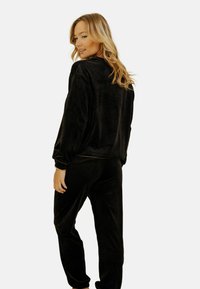 Ensemble de loungewear en velours noir comprenant une veste ample avec un col rond et un pantalon fuselé assorti. Texture douce avec des poignets élastiques.