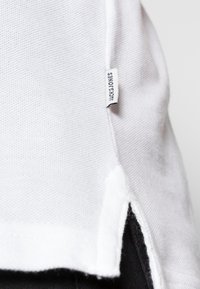 T-shirt blanc à manches courtes en tissu texturé, avec une fente sur le côté et une étiquette "Jack & Jones" cousue sur l'ourlet.
