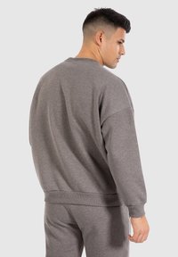 Sweatshirt gris à col ras du cou en tissu doux avec des poignets et un ourlet côtelés. Présente une coupe décontractée et un design minimaliste.