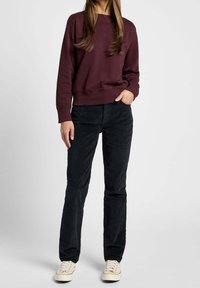 Maroon sweatshirt med rund halsringning, i kombination med svarta kordbyxor. Bär ljusa sneakers. En enkel, avslappnad kläddesign.