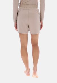 Pantalones cortos beige con cintura elástica, confeccionados en tela suave, con un ajuste relajado y una longitud por encima de la rodilla. Detalles mínimos de costuras visibles.