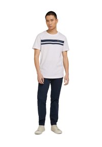 White short-sleeve t-shirt with navy horizontal stripes; paired with navy pants and light-colored sneakers. Simple, casual design.