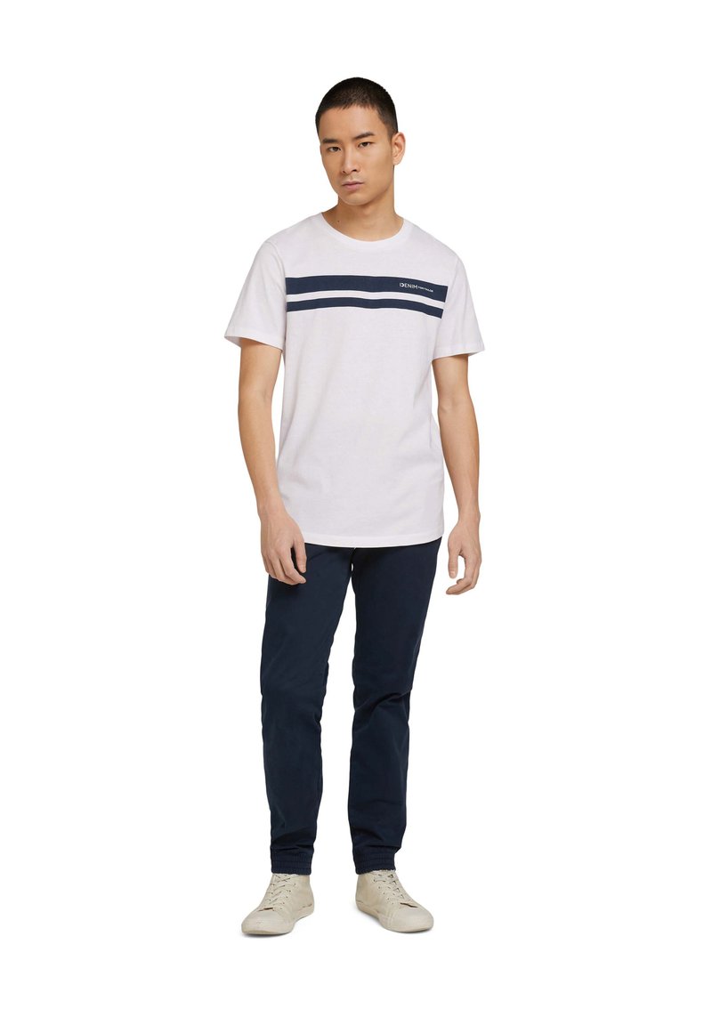White short-sleeve t-shirt with navy horizontal stripes; paired with navy pants and light-colored sneakers. Simple, casual design.