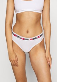 Bikini en coton blanc avec une ceinture en logo "DIESEL" noir et rouge, présentant une texture lisse, un design taille basse et une couverture minimale.