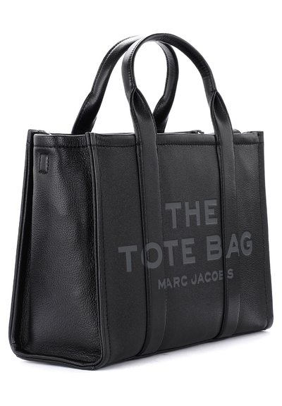 Melna ādas somiņa ar strukturētu dizainu, diviem augšējiem rokturiem, izstieptu tekstu "THE TOTE BAG" un "MARC JACOBS", gludām un tekstūrētām daļām.