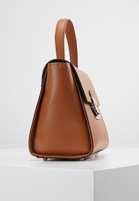 Sac en cuir pebble marron avec une forme structurée, doté d'une anse supérieure, de quincaillerie en argent et d'un accent noir contrastant le long du haut.