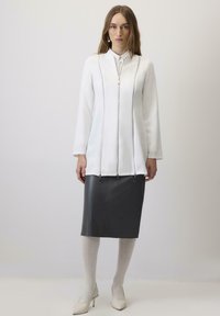 Balta zipa jaka ar garajām piedurknēm, apvienota ar pieguļošu pelēku ādas svārku. Gluda auduma un metāla zipa akcenti piešķir detaļas.