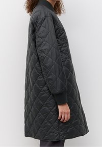 Abrigo largo acolchado negro con cuello y puños acanalados, fabricado en material sintético suave con un patrón de diamantes y bolsillos laterales.